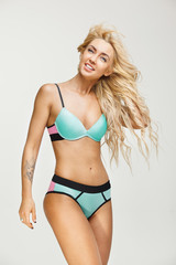 Smiling beautiful woman with blond hair wears bikini on white isolated background. Swimwear season.