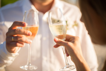 Champagne glasses in the hands of the bride and groom at sunset