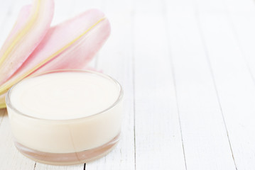 Cosmetic cream and lily flower on white wooden table