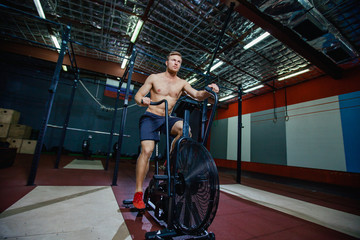 Fit young man using exercise bike at the gym. Fitness male using air bike for cardio workout at cross training gym.