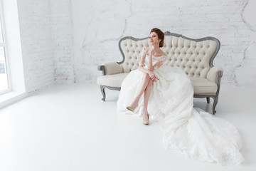 Obraz premium Bride looking out the window, she waits for the groom sitting on big classic sofa. Minimalistic loft studio interior