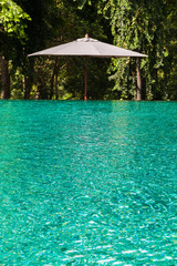 A white umbrella next to clear water in swimming pool