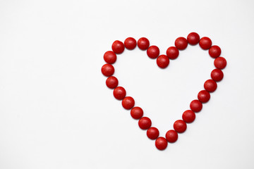 Colorful m&m button chocolate candies in the love shape on white background.