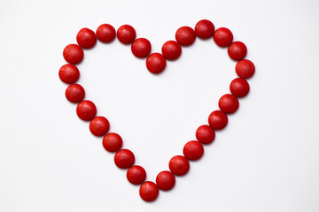Colorful m&m button chocolate candies in the love shape on white background.