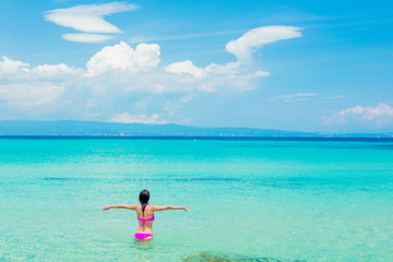 Girl in pink bikini standing in a water on the beach in summertime. Greece