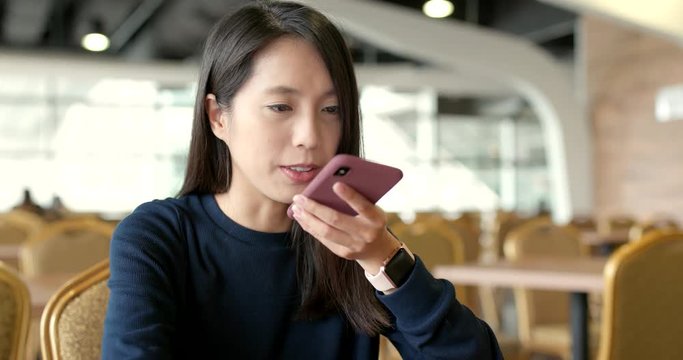 Woman sending audio message on cellphone in restaurant