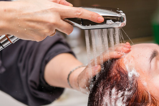 After dyeing hair, the hairdresser washes the girl's hair and washes off the shampoo. Closeup view.