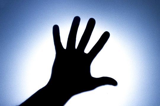 Silhouette of five fingers on a man's hand with a bright light spot. The concept of entreaty for help or greetings. Blue tonality.