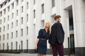 Fototapeta premium Portrait of young couple standing back to each other in the office clothes, on the background of the building