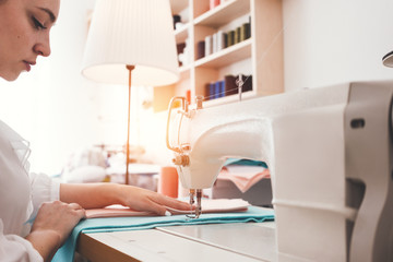 Young dressmaker woman working with cloth on sewing machine in design clothing bureau. Seamstress sew in workshop. Small business