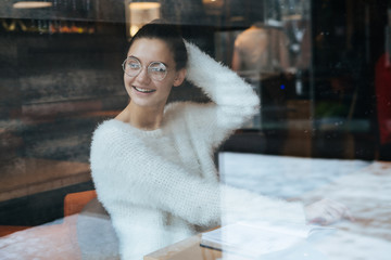 happy young girl freelancer in a white jacket and glasses sitting in a cafe, laughing