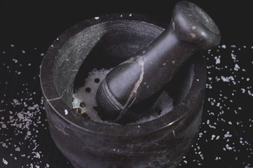 White fish with tomatoes and marble mortar on a black wooden background. Process of cooking