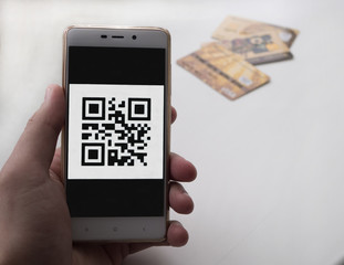 Hand holding smart phone with QR code. 3 bank cards on background