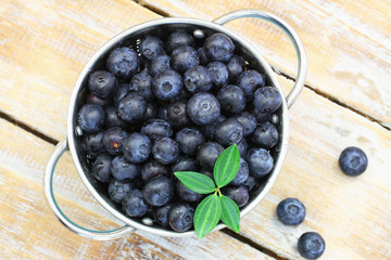 Blueberries in metal colander on rustic wooden surface
