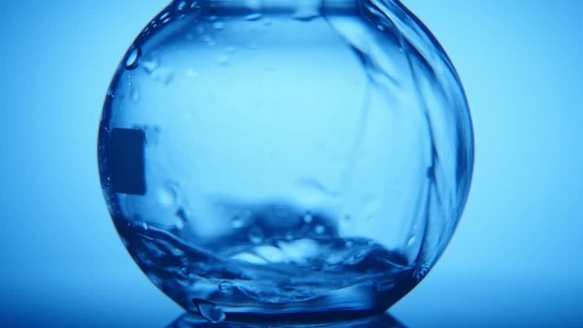 An impressive macro shot of a large round glass flask filled with a narrow stream of crystaline water in the blue background 