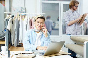Portrait of female designer talking on the phone with her colleague in the background