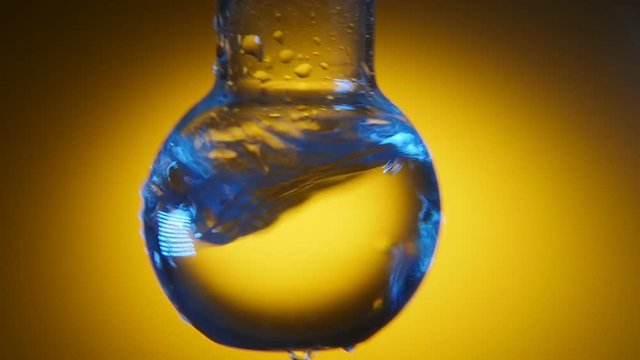 A macro shot of clean water in a round bottom flask shaken in a medical lab. The water plays with blue and yellow shadows.