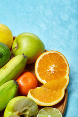 Ripe fresh fruits in a wooden plate on a blue background, selective focus, close-up, top view