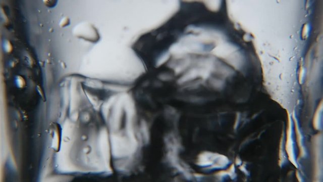   A retro macro shot of several crystaline ice cubes in a moist glass in the grey background. A stream of water is falling later
