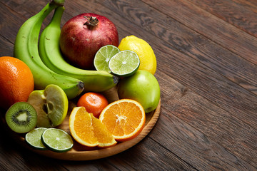 Ripe fresh fruits in a wooden plate on a rustic wooden background, selective focus, close-up, top view