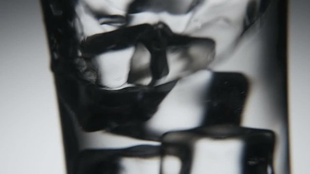 A retro macro shot of gray and white ice cubes shaken stylishly in a sparkling glass with cold water in the grey background.