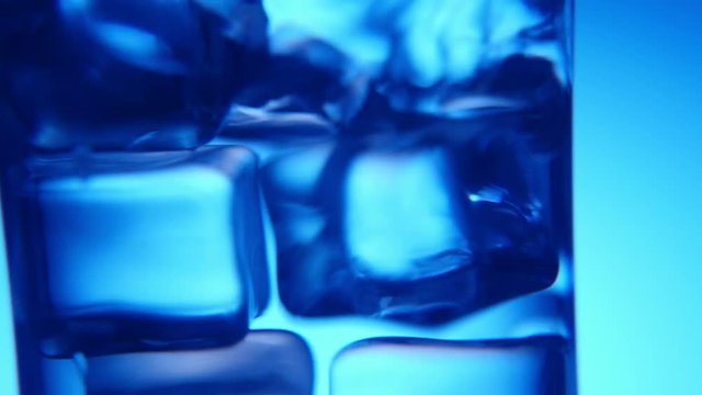 A chic macro shot of five ice cubes dancing elegantly in a sparkling glass with splashing water in the blue background.