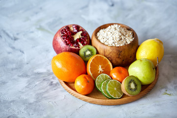 Bowl with oatmeal flakes served with fruits on wooden tray over rustic background, flat lay, selective focus