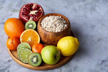 Bowl with oatmeal flakes served with fruits on wooden tray over rustic background, flat lay, selective focus