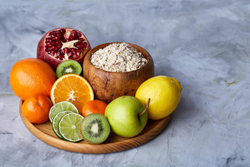 Bowl with oatmeal flakes served with fruits on wooden tray over rustic background, flat lay, selective focus