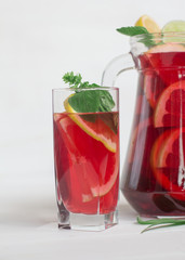 A glass with red sangria and oranges, lime and lemon on a white background. Behind the jug.Close up. Copy-space.