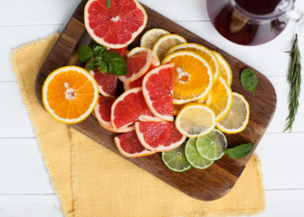 sliced citrus decorated with basil on wooden and white backgrounds with orange towel. Orange, grapefruit, lime, lemon. Flat lay, top view.