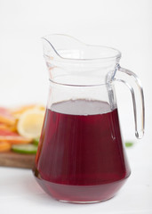 Jug with fruit juice of red color on a white background