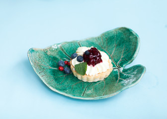 Tart with berry cream and blueberries on a ceramic plate on a blue background