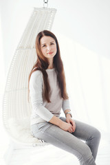 Young cute long-haired brunette sits in a hanging white chair