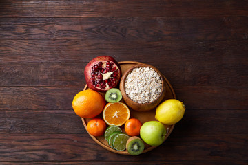 Bowl with oatmeal flakes served with fruits on wooden tray over rustic background, flat lay, selective focus