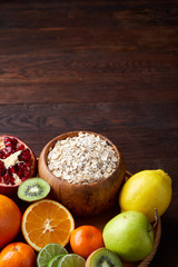 Bowl with oatmeal flakes served with fruits on wooden tray over rustic background, flat lay, selective focus