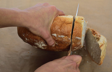 Closeup of a chef hands holding  knife for cut fresh home bread on parchment for baking with .  Fresh bread on the kitchen table The healthy eating and traditional bakery 