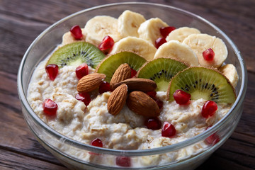 Delicious oatmeal porrige with fruits in glass bowl over rustic wooden background, shallow depth of field, close-up.
