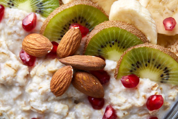 Delicious oatmeal porrige with fruits in glass bowl over rustic wooden background, shallow depth of field, close-up.