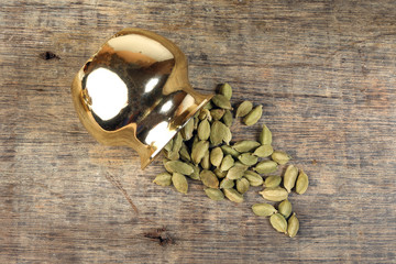 Cardamom spice in golden metal pot on rustic wood