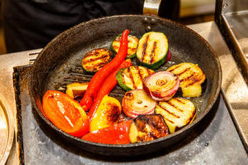 Grilled vegetables are fried on a frying pan: pepper, zucchini, onion.