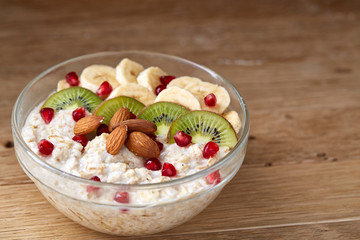 Delicious oatmeal porrige with fruits in glass bowl over rustic wooden background, shallow depth of field, close-up.