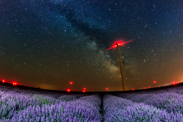 Beautiful starry night sky with milky way over a field of lavender and red lights of wind turbines,...