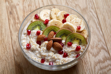 Delicious oatmeal porrige with fruits in glass bowl over rustic wooden background, shallow depth of field, close-up.