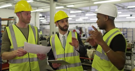 Warehouse workers discuss the logistics of their business while looking at a digital tablet.