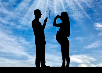 Silhouette of a man egoist smoking near a pregnant woman. She covered her nose with her hand from...