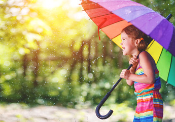 Happy child girl laughs and plays under summer rain with an umbrella.