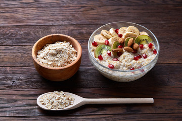 Bowl with oatmeal flakes served with fruits on wooden tray over rustic background, flat lay, selective focus