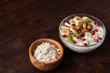 Bowl with oatmeal flakes served with fruits on wooden tray over rustic background, flat lay, selective focus