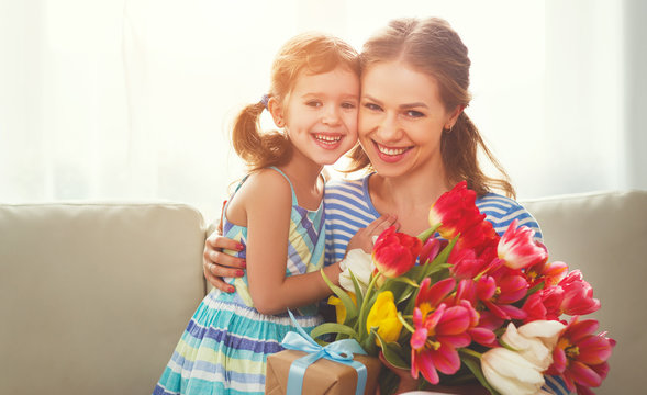 happy mother's day! child daughter   gives mother a bouquet of flowers to tulips and gift